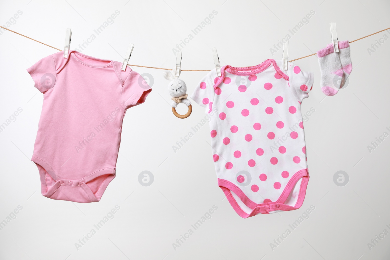 Photo of Cute baby onesies, socks and crochet toy drying on washing line against white background