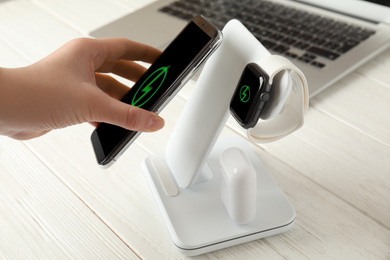 Woman putting mobile phone onto wireless charger at white wooden table, closeup
