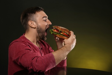 Young man eating tasty burger on color background. Space for text