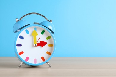 Photo of Alarm clock on white wooden table against light blue background, space for text