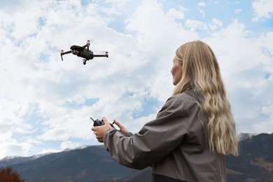 Photo of Young woman operating modern drone with remote control in mountains