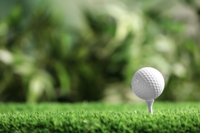 Photo of Golf ball with tee on artificial grass against blurred background, space for text