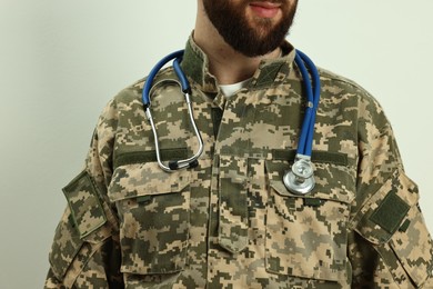 Man in military uniform with stethoscope on light background, closeup. Health care concept