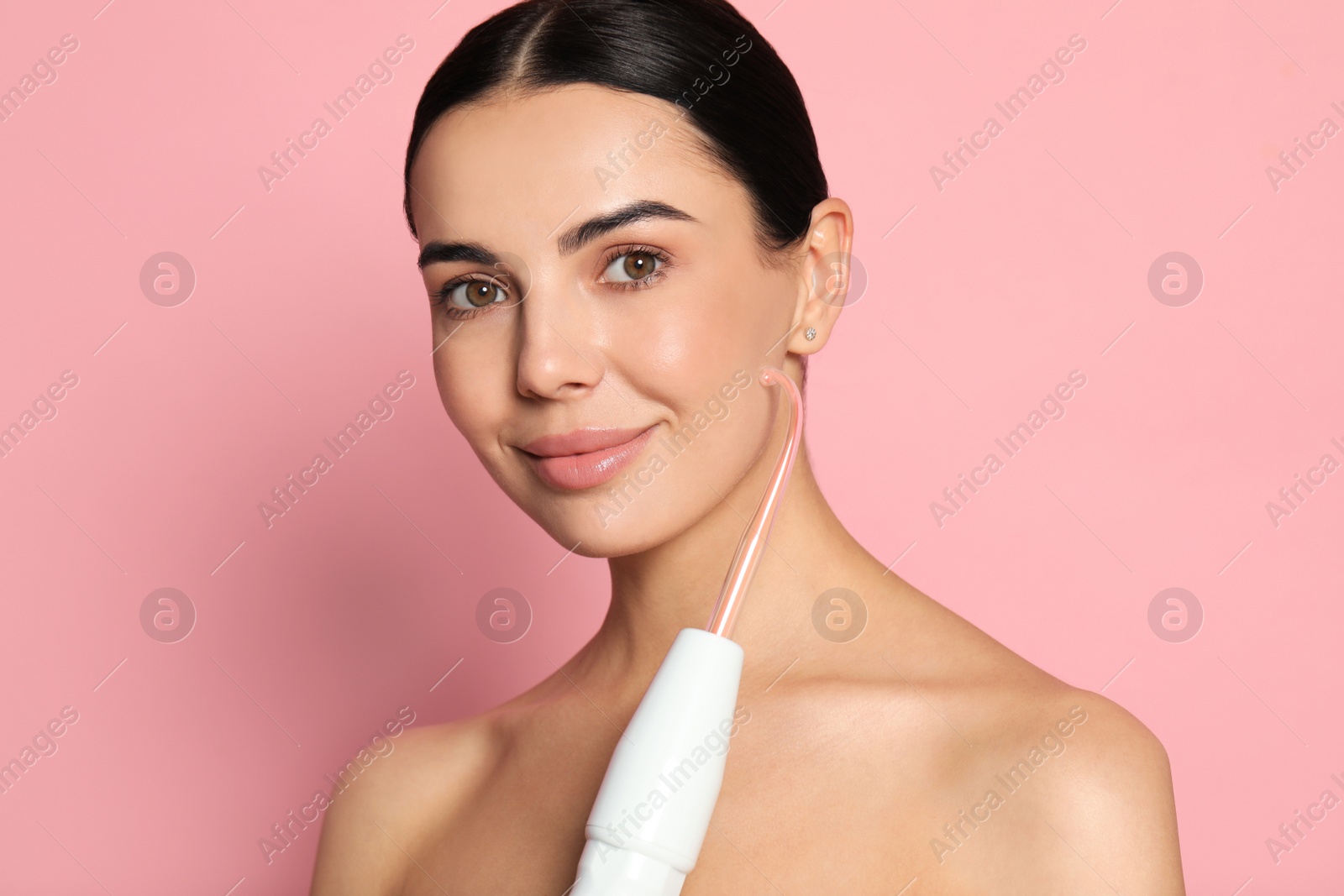 Photo of Woman using high frequency darsonval device on pink background