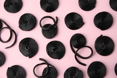 Tasty black liquorice candies on pink background, flat lay