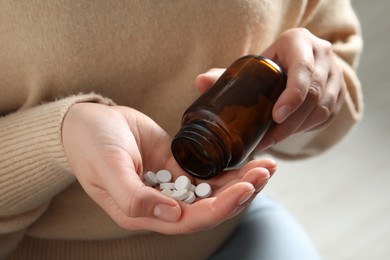 Photo of Woman pouring pills from bottle on light background, closeup