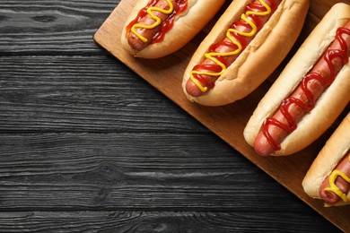 Photo of Delicious hot dogs with mustard and ketchup on black wooden table, top view. Space for text