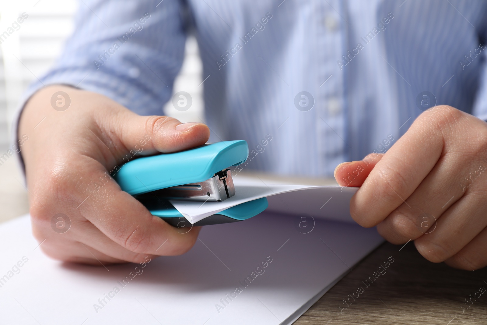 Photo of Woman stapling papers at wooden table indoors, closeup