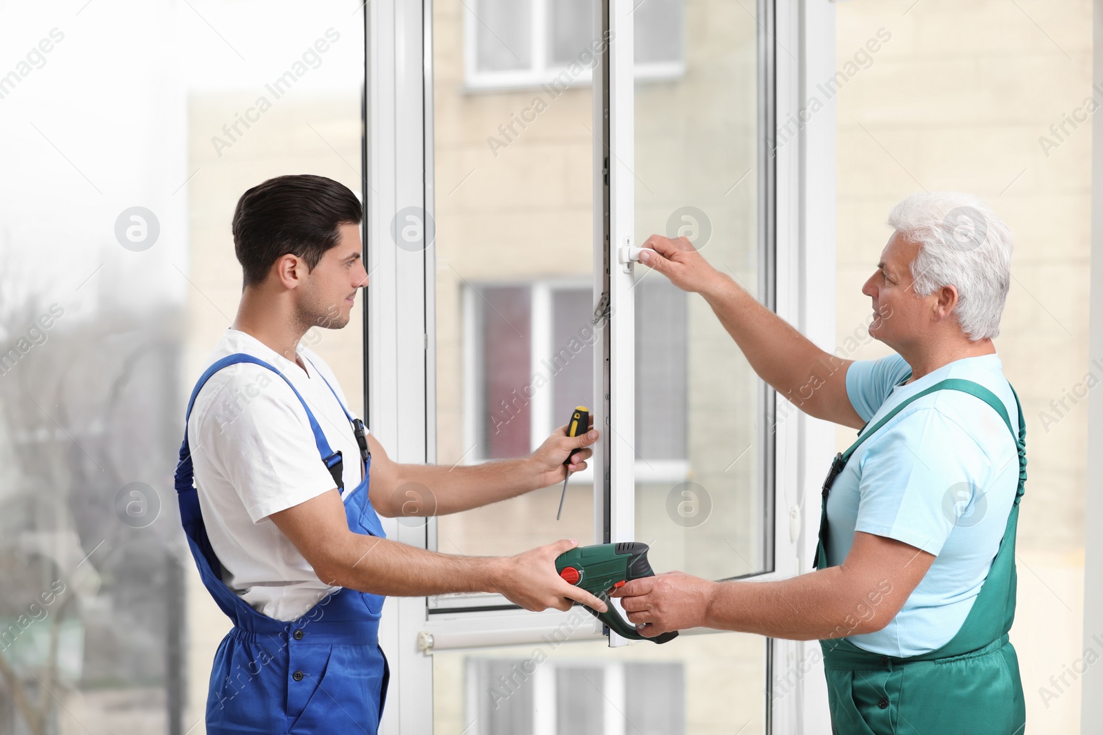 Photo of Construction workers repairing plastic window with screwdriver indoors