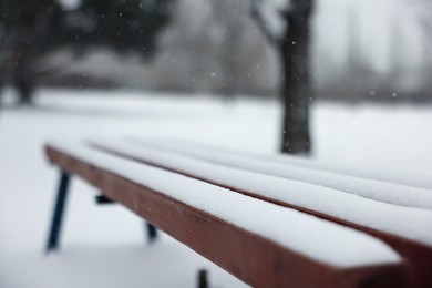 Bench covered with snow in city park, closeup