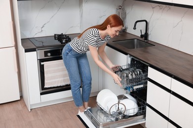 Smiling woman loading dishwasher with cutlery in kitchen