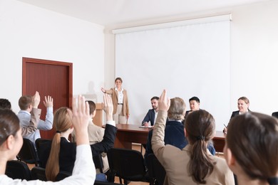 People raising hands to ask questions at business conference in meeting room