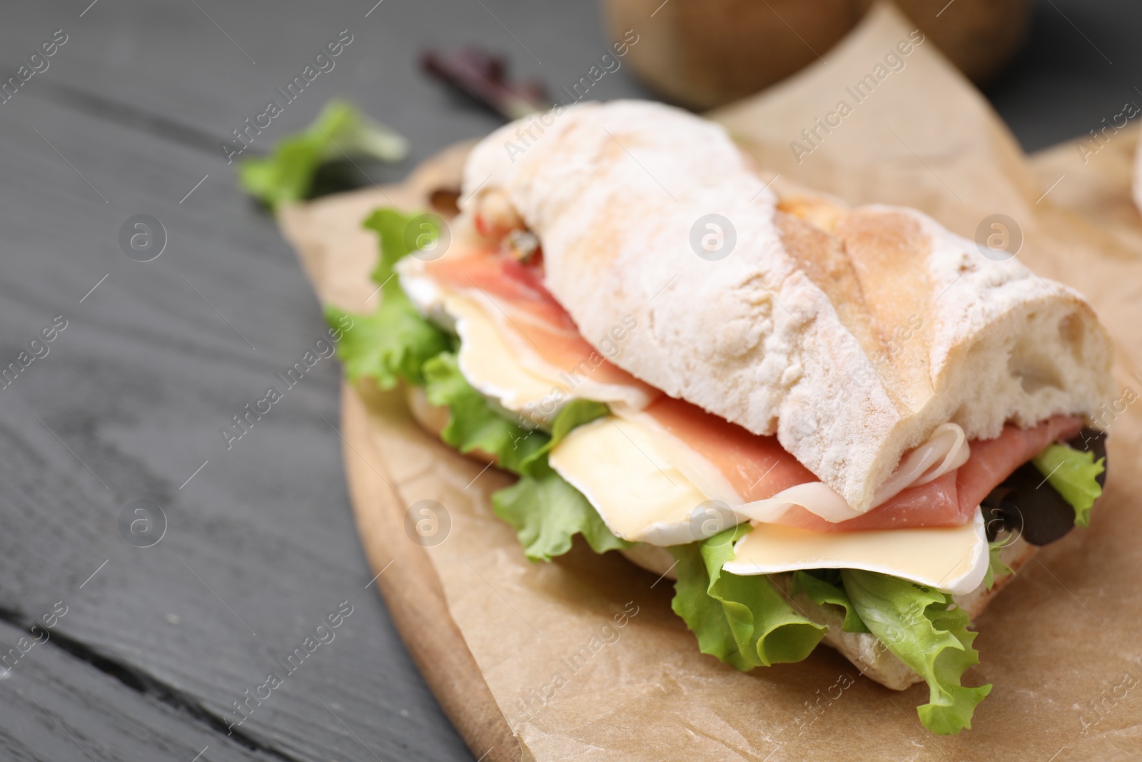 Photo of Tasty sandwich with brie cheese and prosciutto on grey wooden table, closeup. Space for text