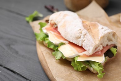 Tasty sandwich with brie cheese and prosciutto on grey wooden table, closeup. Space for text