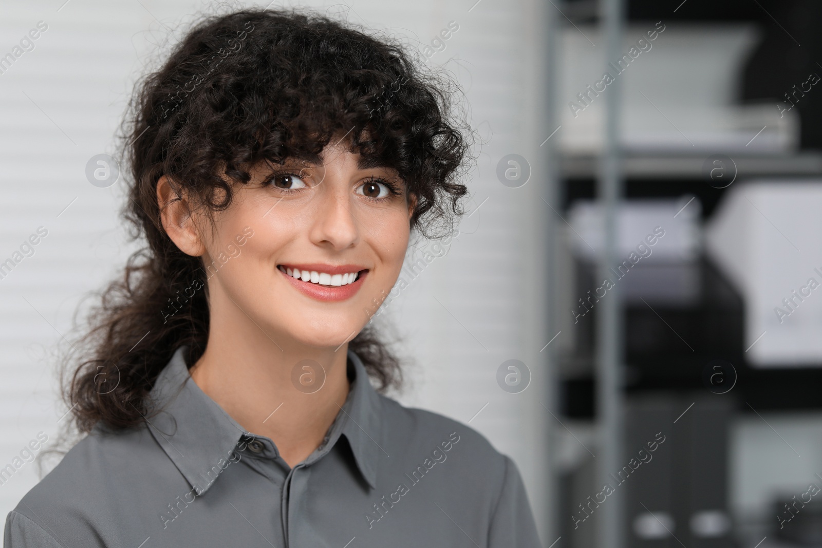 Photo of Portrait of confident entrepreneur indoors. Beautiful lady with curly hair smiling and looking into camera. Space for text