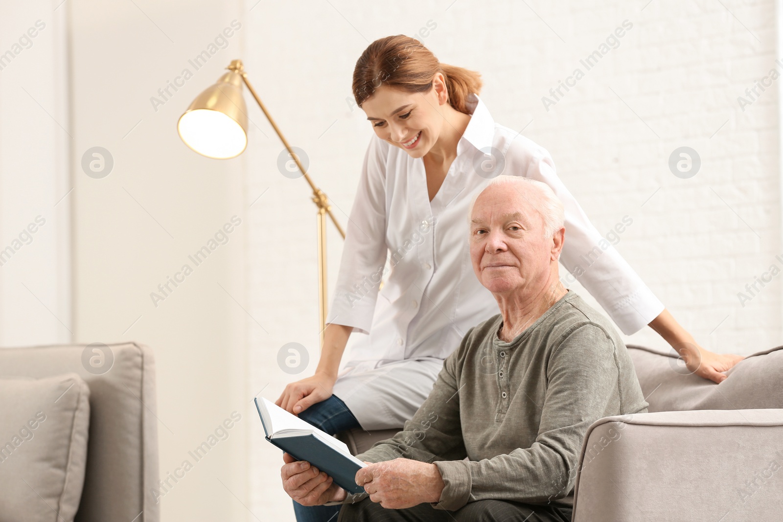 Photo of Elderly man with female caregiver in living room. Space for text