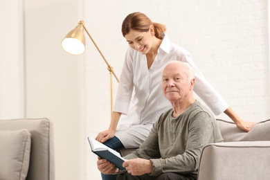 Elderly man with female caregiver in living room. Space for text