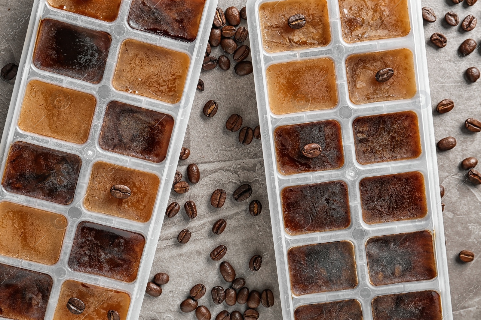 Photo of Ice cubes in trays and coffee beans on grey background, flat lay