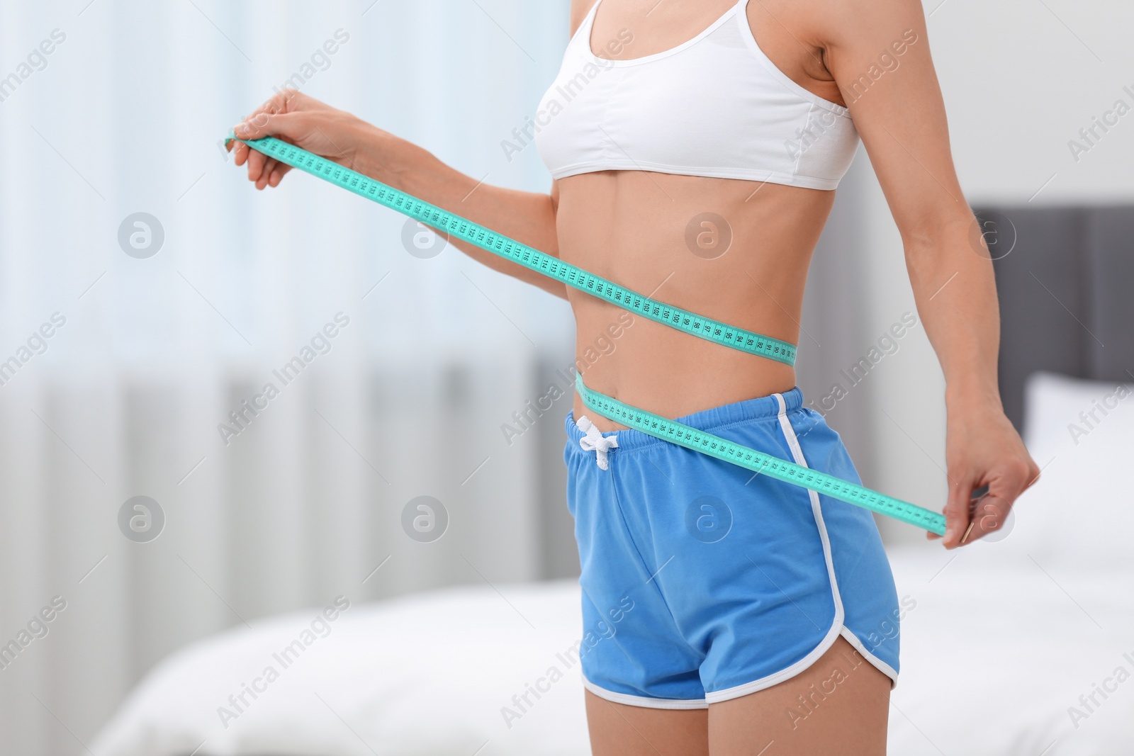 Photo of Slim woman measuring waist with tape at home, closeup and space for text. Weight loss