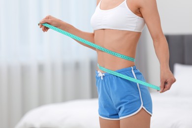 Photo of Slim woman measuring waist with tape at home, closeup and space for text. Weight loss