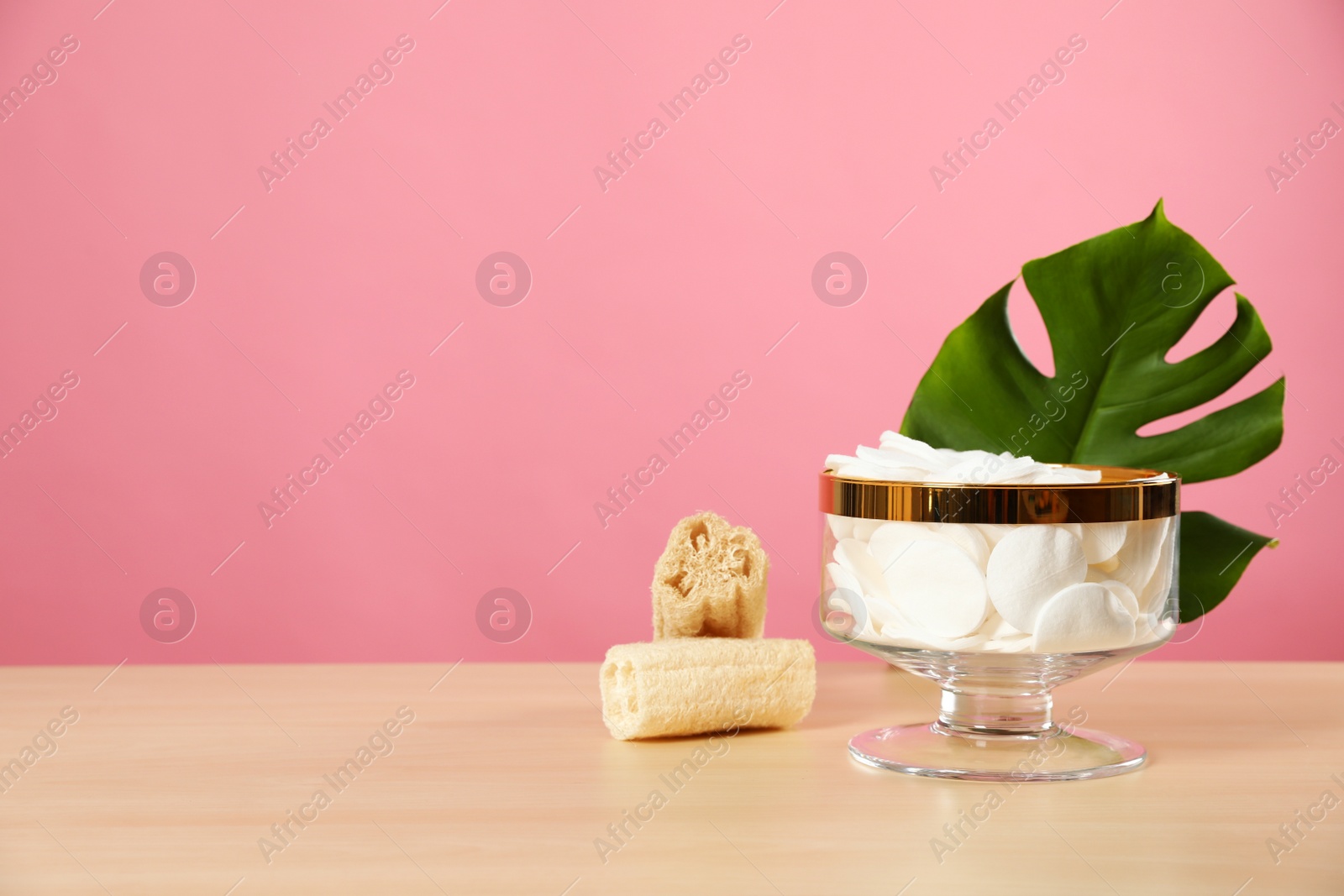 Photo of Jar with cotton pads on wooden table against pink background. Space for text