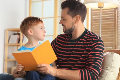 Photo of Father reading book with his son in living room at home