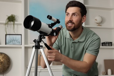 Photo of Handsome man using telescope to look at stars in room