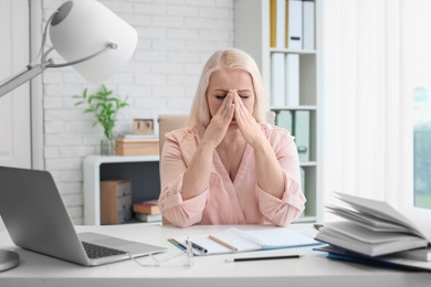 Mature woman suffering from headache while sitting at table in office