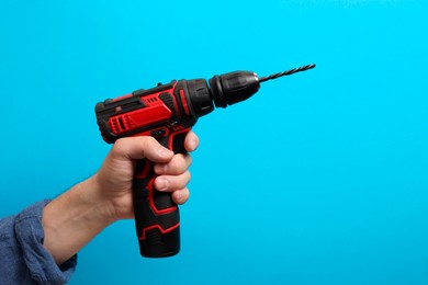 Photo of Handyman holding electric screwdriver on light blue background, closeup