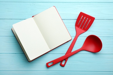 Photo of Soup ladle, spatula and empty recipe book on wooden  background, top view