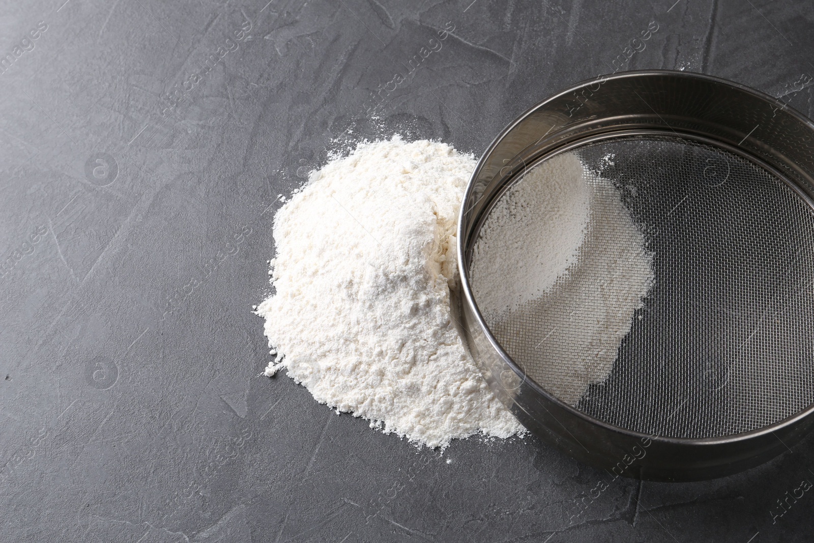 Photo of Metal sieve and flour on grey table. Space for text