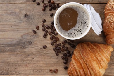 Photo of Coffee to go. Paper cup of tasty drink, croissants and beans on wooden table, flat lay with space for text