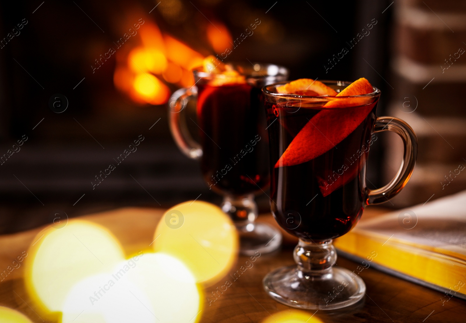 Photo of Tasty mulled wine, festive lights and blurred fireplace on background