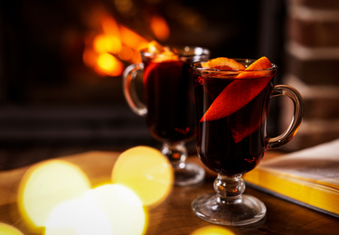 Photo of Tasty mulled wine, festive lights and blurred fireplace on background