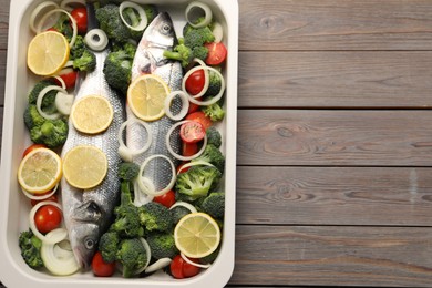 Photo of Raw fish with vegetables and lemon in baking dish on wooden table, top view. Space for text