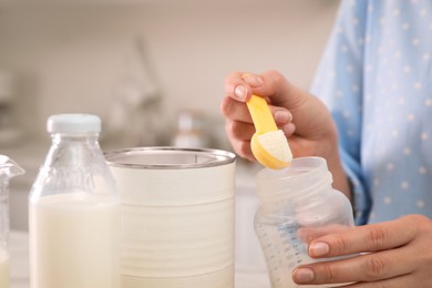 Photo of Woman preparing infant formula indoors, closeup. Baby milk