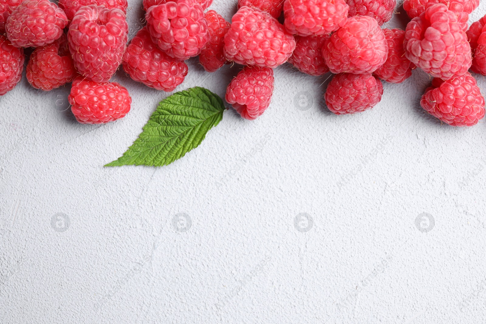 Photo of Fresh ripe raspberries with green leaf on light grey table, top view. Space for text