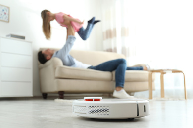 Photo of Man and his daughter having fun while robotic vacuum cleaner doing its work at home