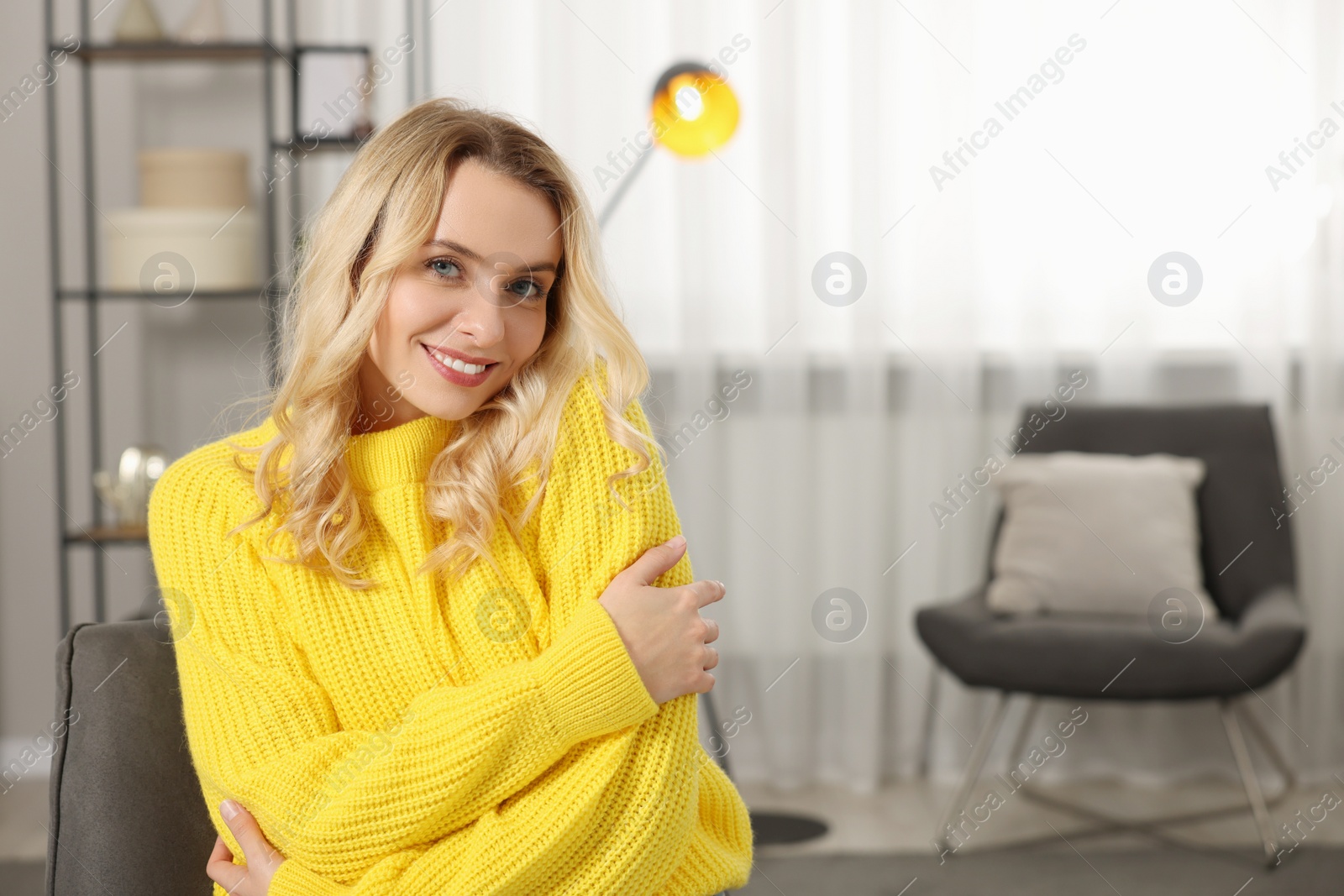 Photo of Happy woman wearing stylish warm sweater in armchair at home. Space for text