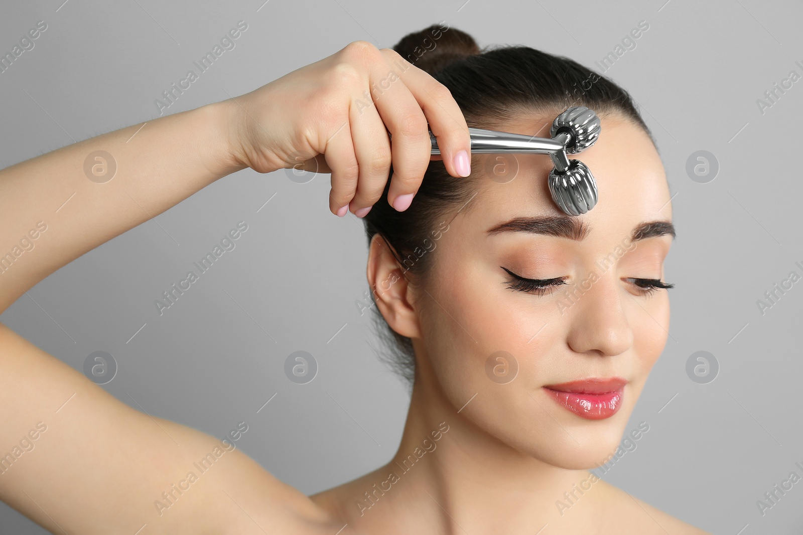 Photo of Woman using metal face roller on grey background