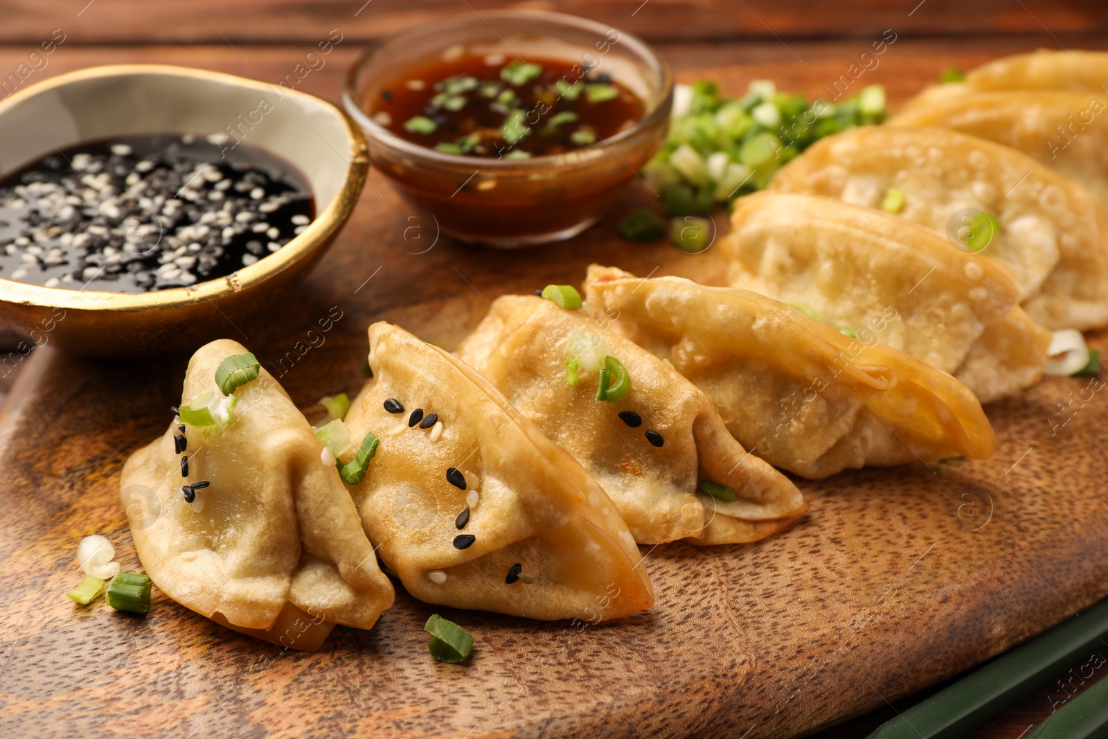 Photo of Delicious gyoza (asian dumplings) with sesame seeds and green onions on wooden board, closeup