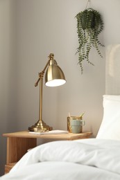 Stylish golden lamp and stationery on wooden nightstand in bedroom. Interior element
