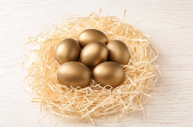 Golden eggs in nest on wooden background