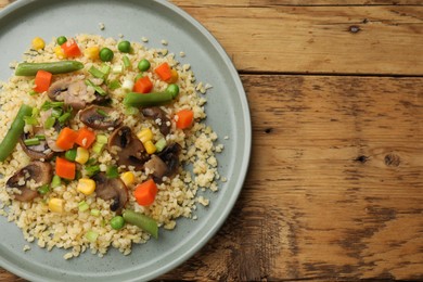 Delicious bulgur with vegetables and mushrooms on wooden table, top view. Space for text