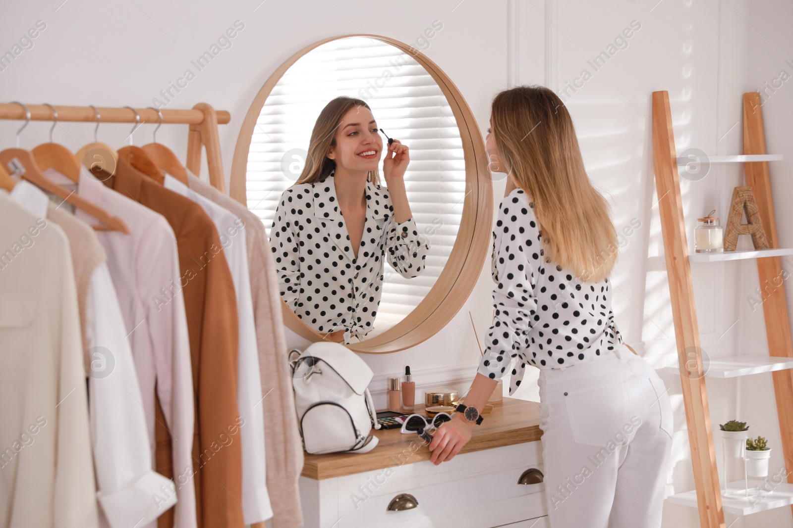 Photo of Young woman doing makeup near mirror at home. Morning routine
