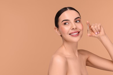 Photo of Beautiful young woman holding skincare ampoule on beige background. Space for text