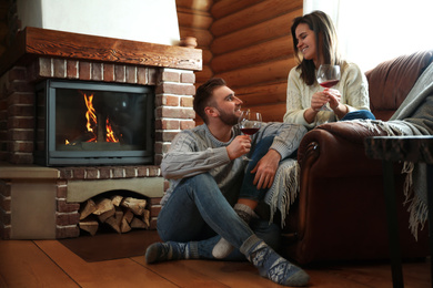 Lovely couple with glasses of wine near fireplace indoors. Winter vacation