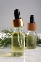 Photo of Bottles of essential oil and fresh dill on white table, closeup