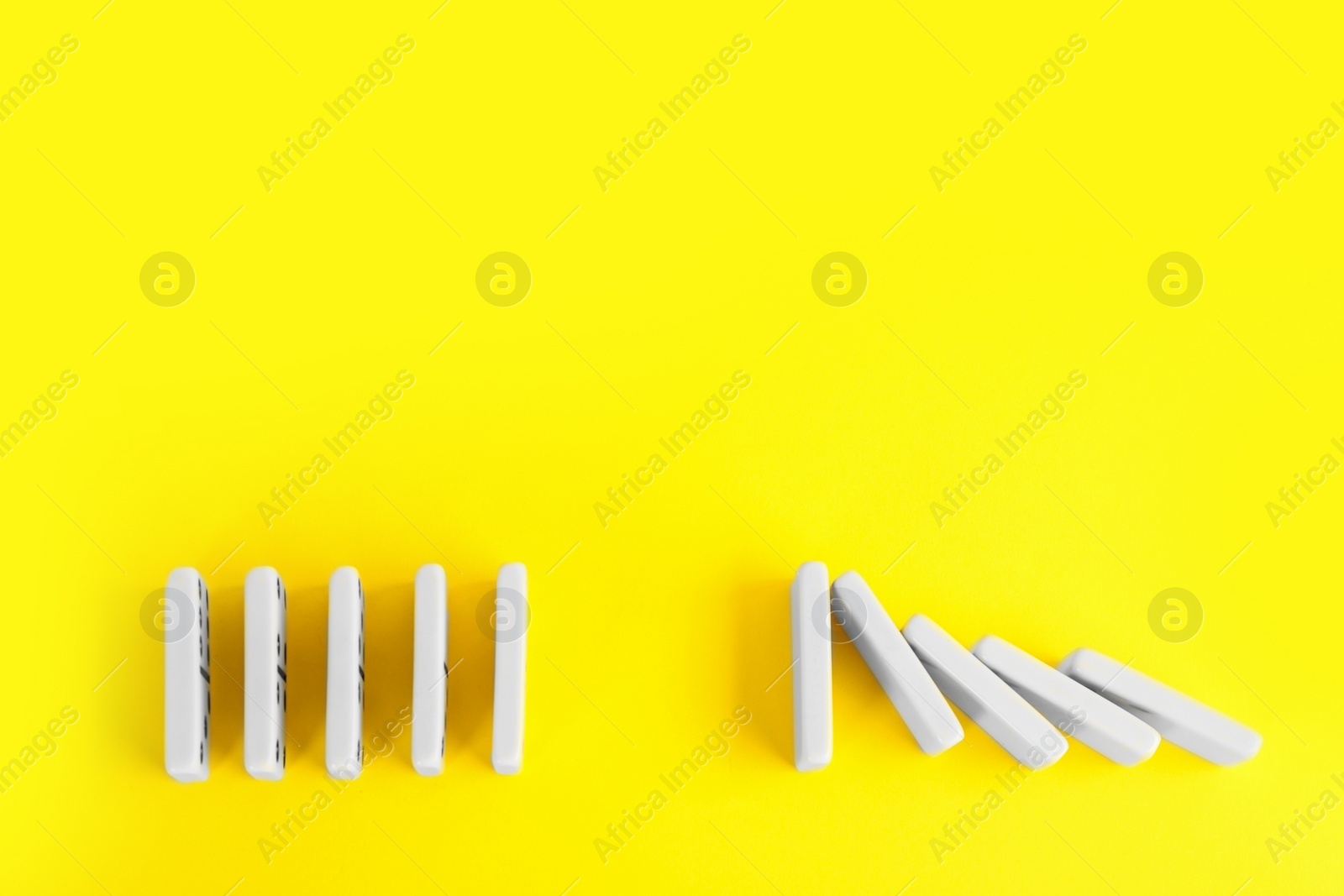 Photo of White domino tiles on yellow background, flat lay. Space for text