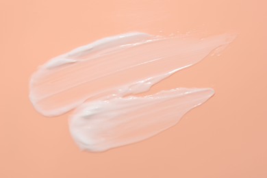 Photo of Samples of face cream on coral background, top view